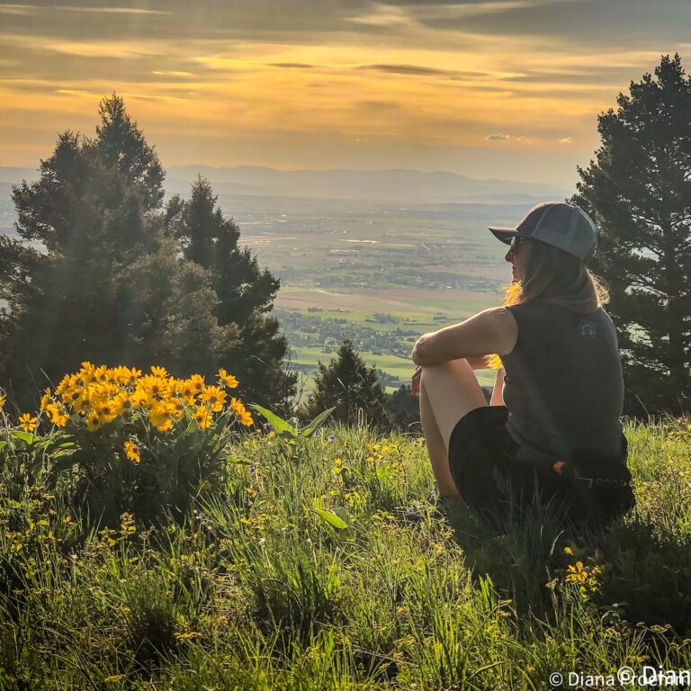A woman over 50 looking out over a mountain valley while hiking alone on a rugged trail.